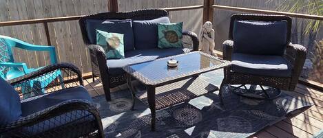 A covered patio with wicker furniture, a glass coffee table, and a view of a house.