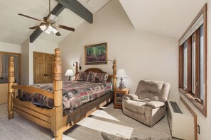 A bedroom with a four-poster bed, a wooden chair, a painting, and a window.