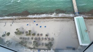 An aerial view of a beach with umbrellas, lounge chairs, and palm trees.
