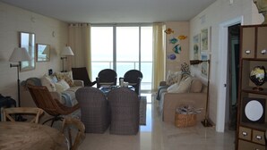 A spacious living room with a large window, wicker furniture, and a view of the ocean.