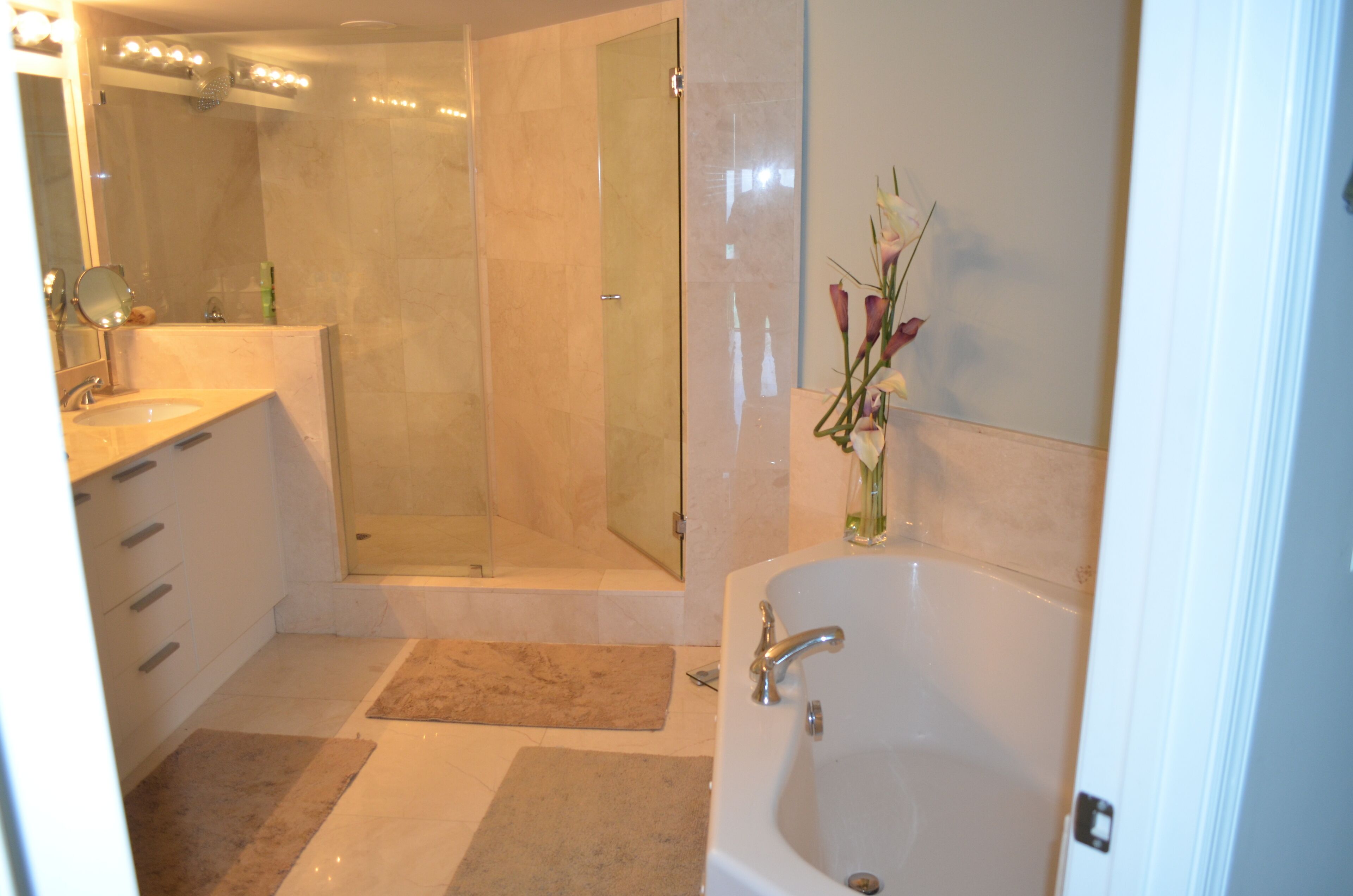 Ein modernes Badezimmer mit einer gläsernen Duschkabine, einer großzügigen Badewanne und einem Waschtisch mit Spiegel.
