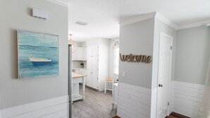 Una cocina con armarios blancos, piso de madera y un cuadro de un barco en la pared.