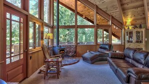Un vaste espace de vie doté de grandes fenêtres, d’une cheminée, de meubles en cuir et d’un plafond en bois.