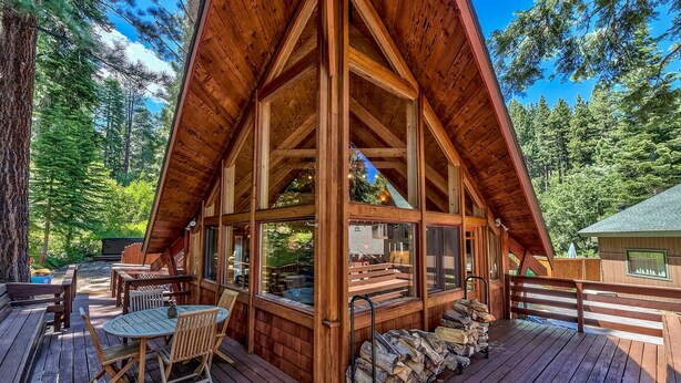 Une cabane en bois dotée d’une grande terrasse, de sièges intégrés et offrant une vue sur la forêt environnante.