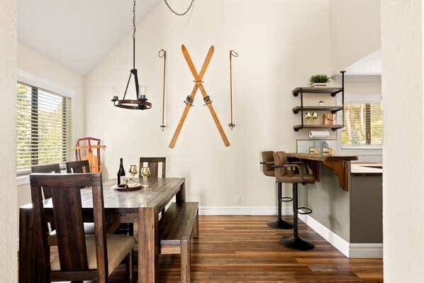 A dining area with a wooden table and chairs, a chandelier, and skis mounted on the wall. - Lux Cabin Retreat: Outdoor Soaking Tubs, Sauna, Firepit, Game Room for kids (Lake Arrowhead)
