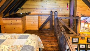 Un dormitorio acogedor en el ático con suelo de madera, una cama con colcha floral, un escritorio pequeño y una escalera con barandilla.