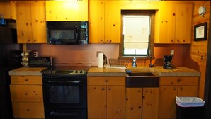 Una cocina compacta con gabinetes de madera, un microondas, una estufa, un fregadero y un ventanal.