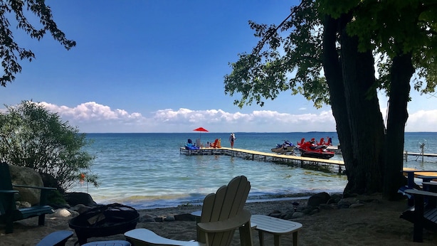 A beachside area with a wooden pier extending into the water, featuring a red umbrella and seating. - Truly a slice of heaven a must see! (Innisfil)