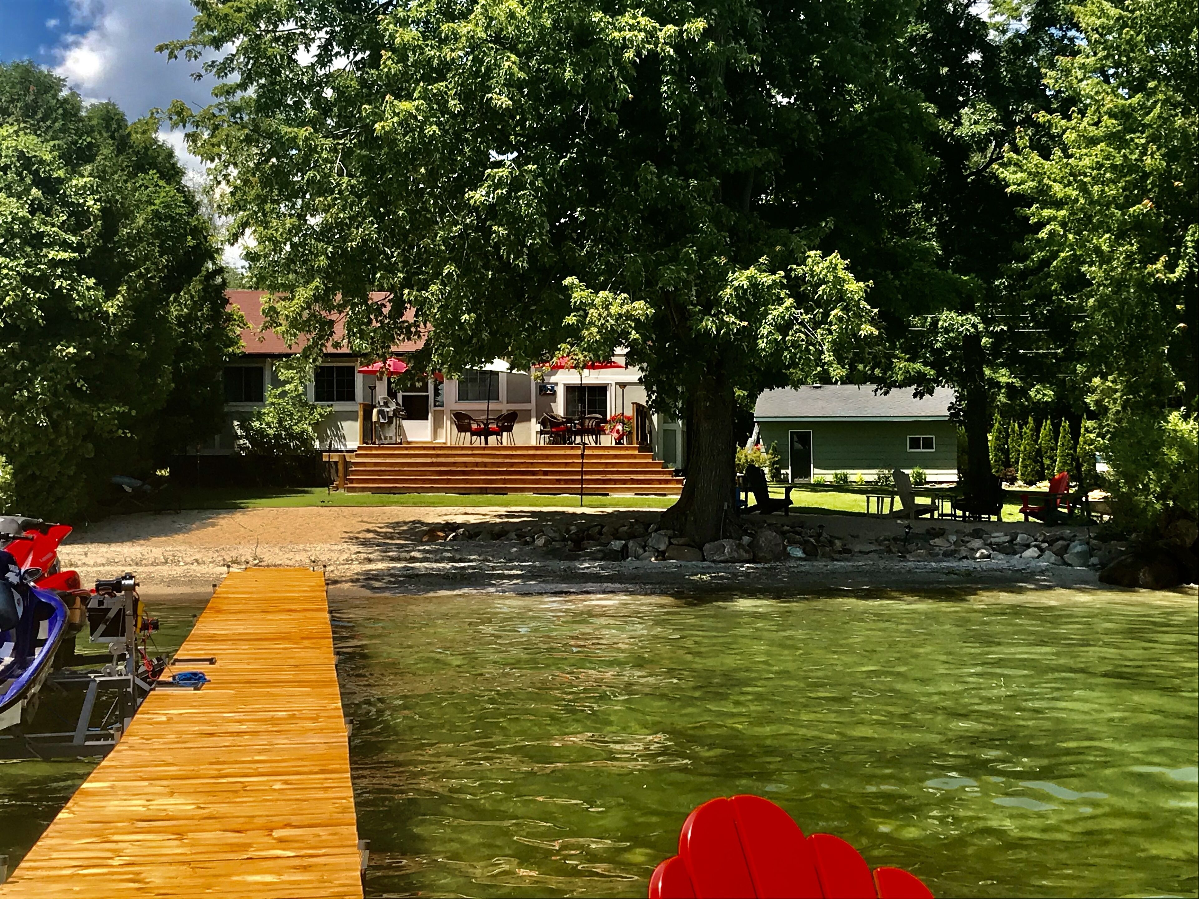 A wooden dock extending into a clear body of water, with a building featuring outdoor seating and a staircase leading up to it.
