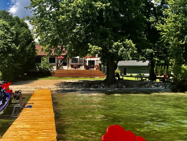 A wooden dock extending into a clear body of water, with a building featuring outdoor seating and a staircase leading up to it.