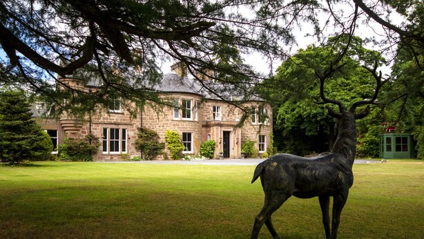 A stone building with a large lawn and a statue of a deer in front.