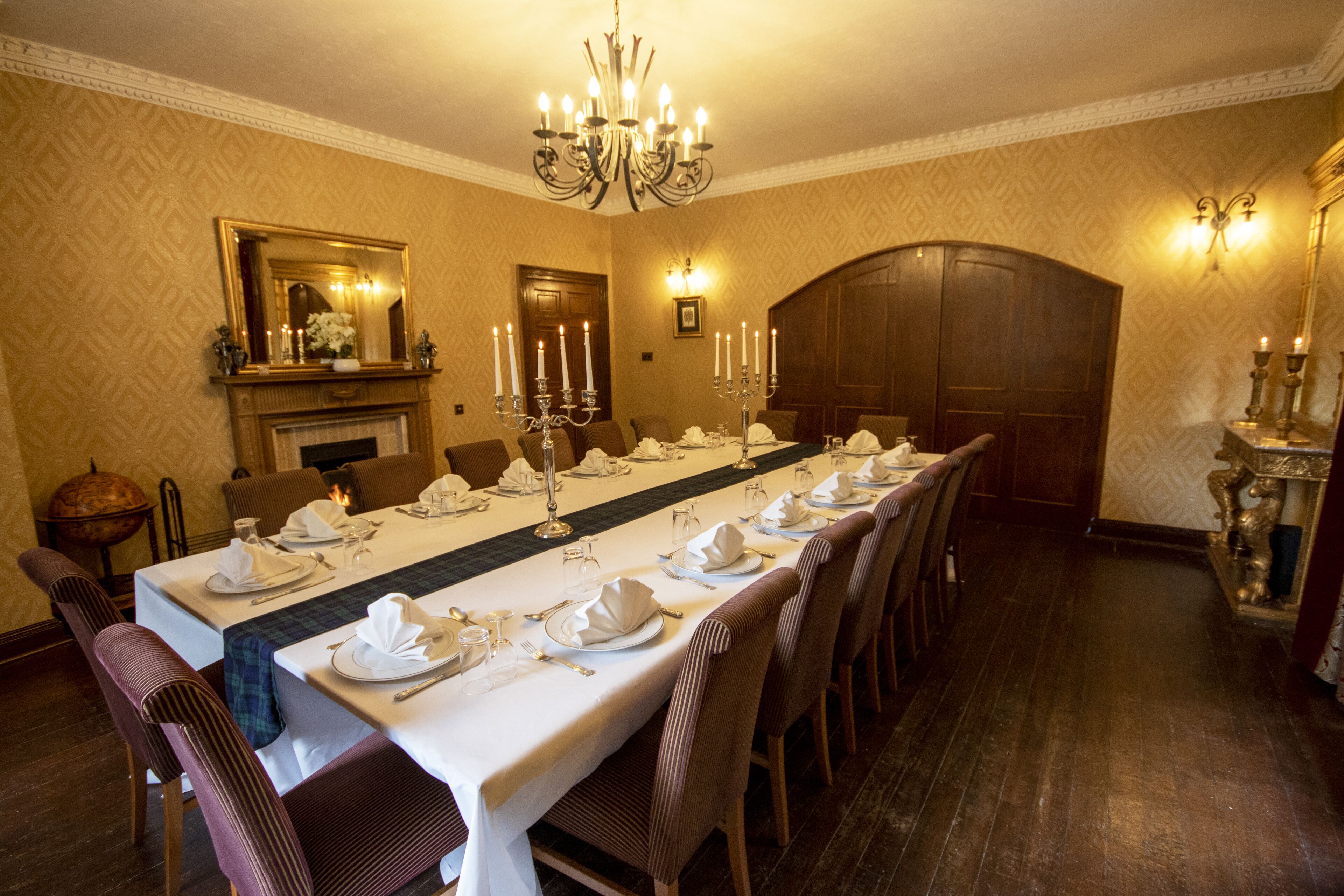A formal dining room with a long table set for a meal, a chandelier, and a fireplace.