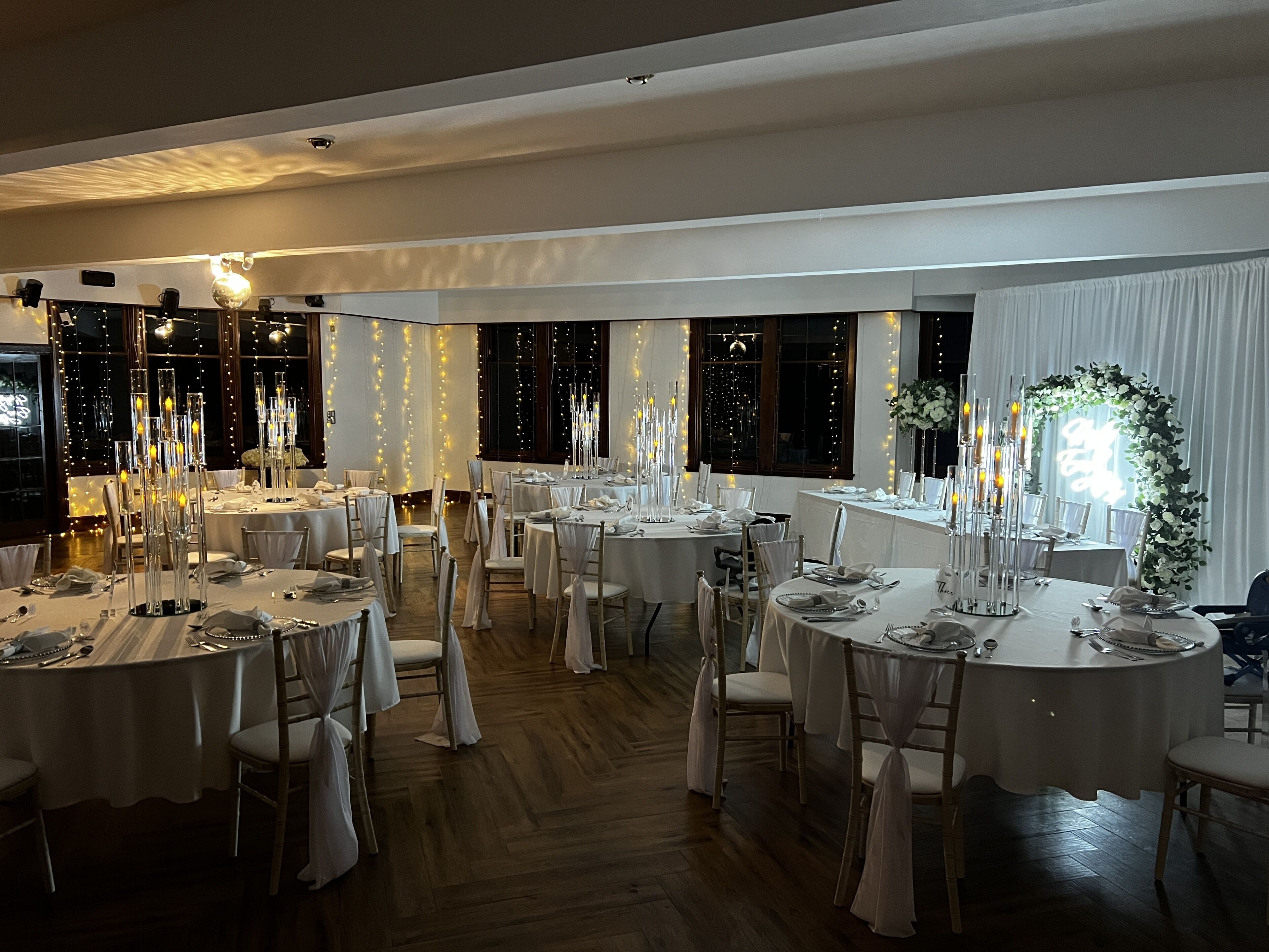 Un salón de banquetes con mesas redondas dispuestas para comer, cortinas blancas y altos centros de mesa con forma de velas.