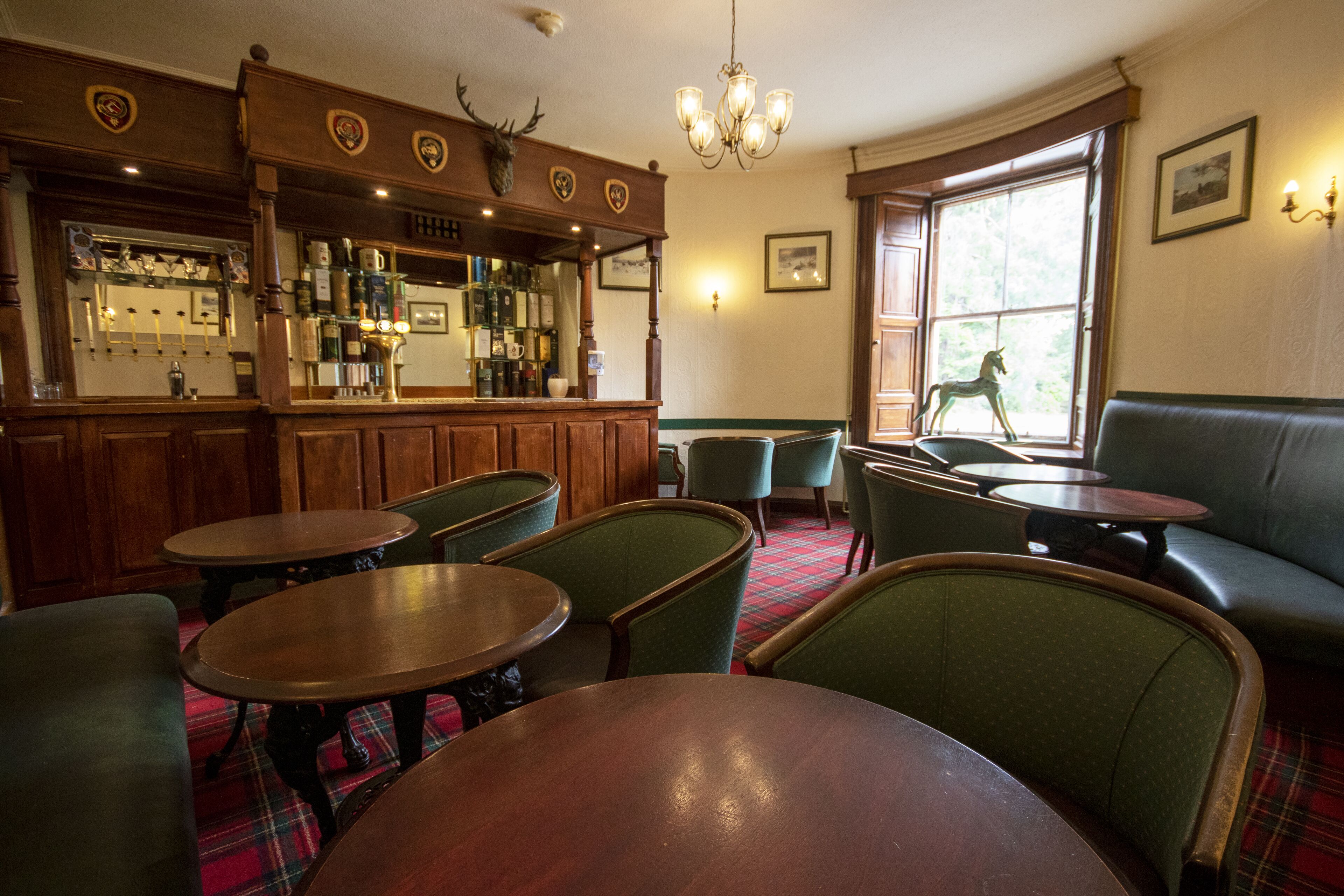 A bar area with wooden furniture, a green upholstered sofa, and a window with a view of a deer statue.