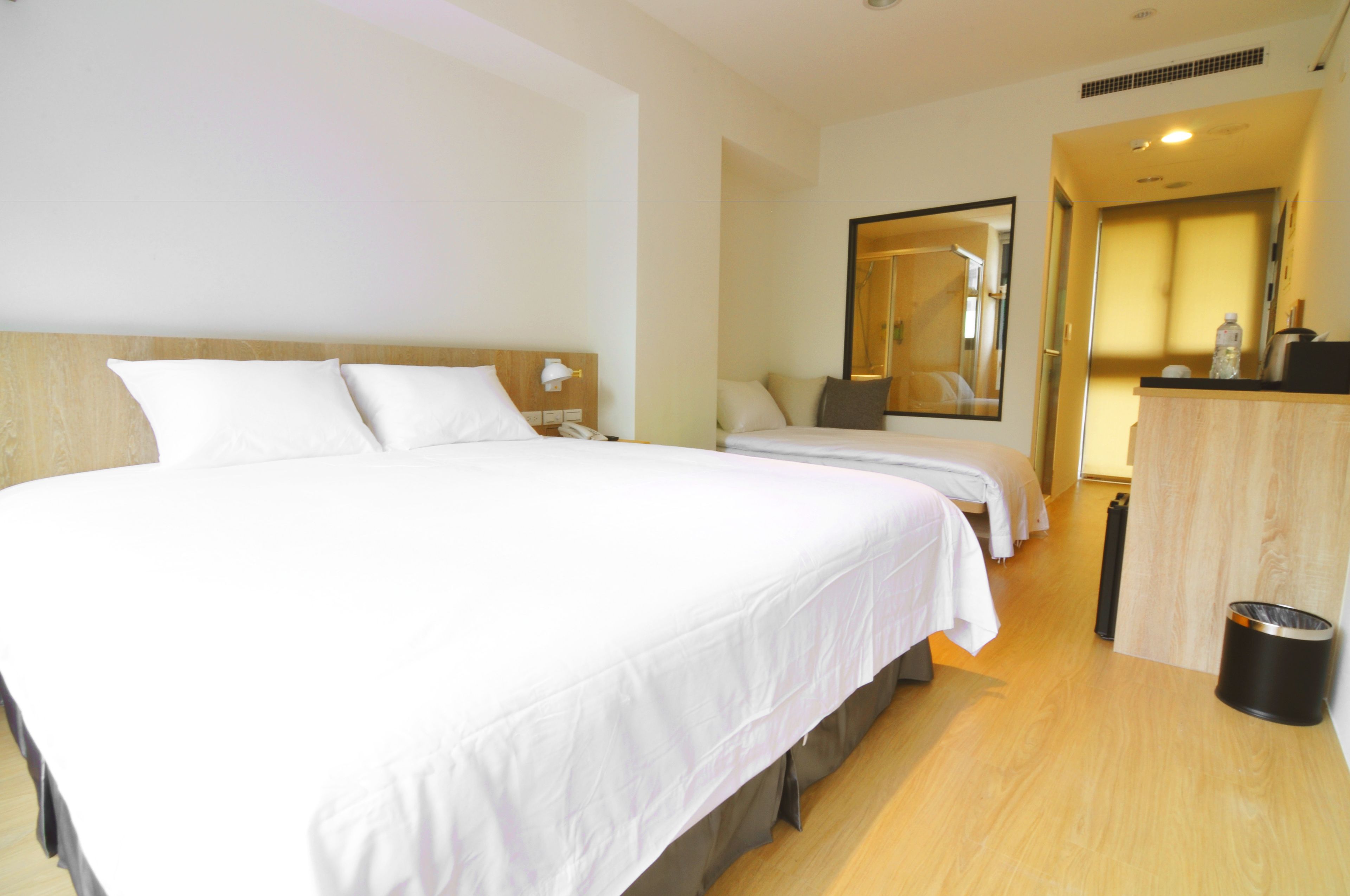 A hotel room with a large bed, two bedside tables, a mirror, and a wooden desk.