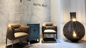 Moderni hotellin aula, jossa on kaksi nahkaista nojatuolia, sininen kaappi ja koristeellinen maljakko.