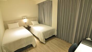 A hotel room with two single beds, a desk with a chair, a nightstand with a lamp, and a large window with curtains.