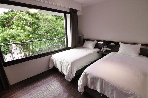 A hotel room with two beds, a large window with a view of greenery, and a wooden floor. - Hotelkuei (Taichung)