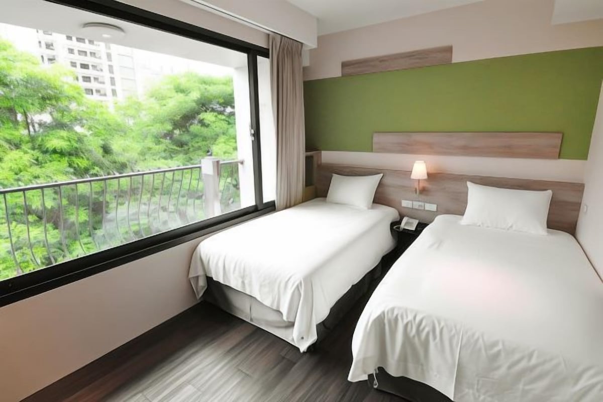 Ein Hotelzimmer mit zwei Betten, Blick auf Grünfläche und modernem Design mit grüner Akzentwand.