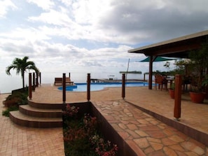 A pool area with steps leading to a patio, surrounded by potted plants and wooden furniture. - Fare Vai Nui (Raiatea)