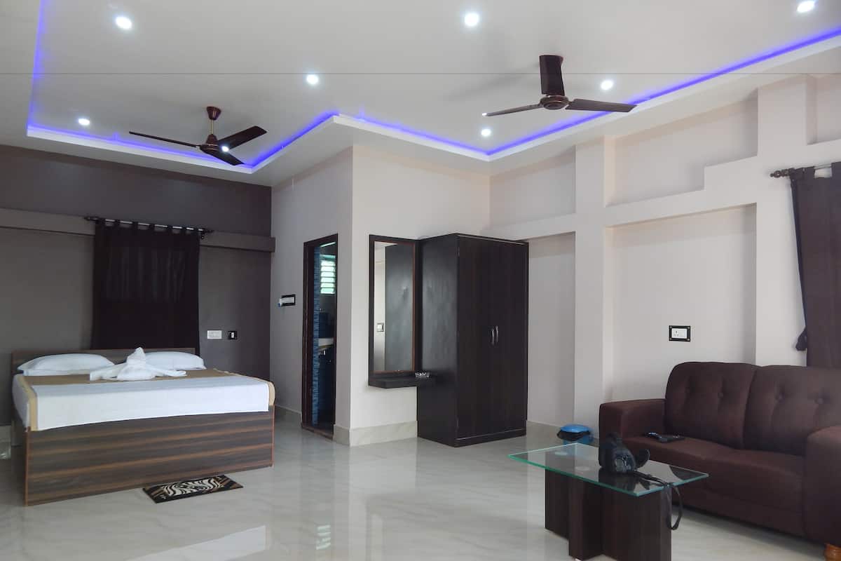 Quarto de hotel moderno com cama, sofá, mesa de centro de vidro, guarda-roupa e ventilador de teto.