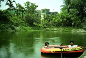 Two people on an inflatable tube in a river surrounded by lush greenery and buildings in the background.