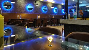 A restaurant interior with round mirrors on the wall, tables, chairs, and hanging pendant lights. - Samriddhi Banquet Garden & Resort (Baharampur)