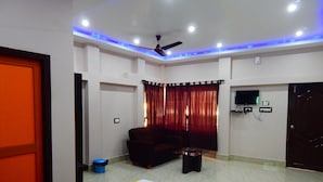 A hotel room with a bed, a sofa, a TV, and a ceiling fan. - Samriddhi Banquet Garden & Resort (Baharampur)