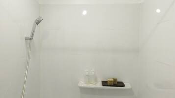 A white shower stall with a handheld showerhead, a soap dispenser, and a soap bar on a shelf.