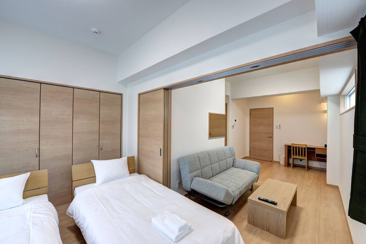 A hotel room with two beds, a grey sofa, a wooden desk, and a small wooden table.