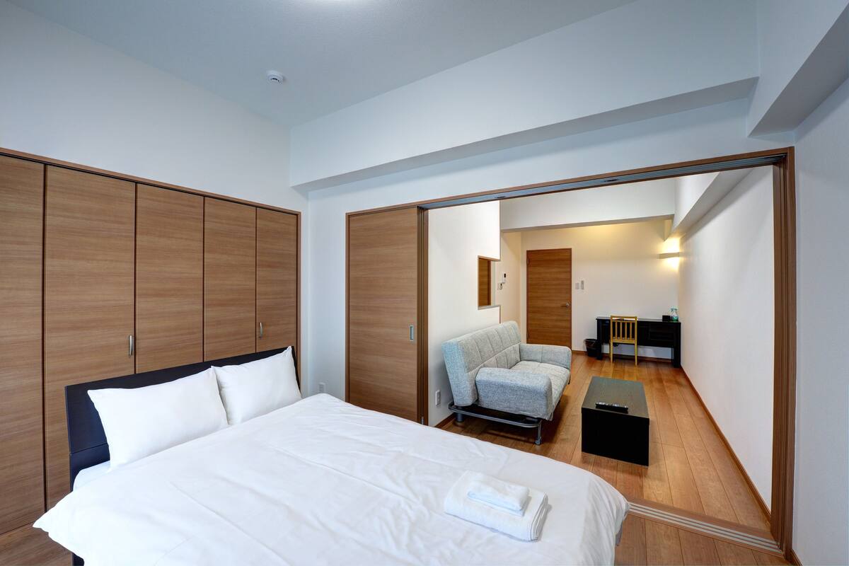A modern hotel room with a large bed, a seating area with a chair and a table, and a wardrobe.