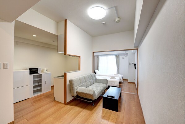 Quarto moderno e bem iluminado, com sofá, pequena mesa e área de kitchenette.