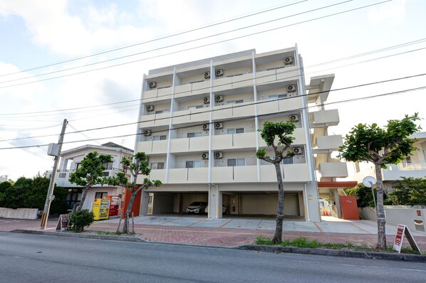 A multi-story building with a parking garage, air conditioning units, and a few trees.