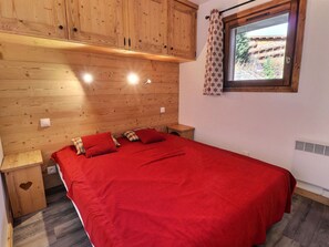 A wooden-paneled room with a bed, wooden nightstands, a window with a view, and a radiator.