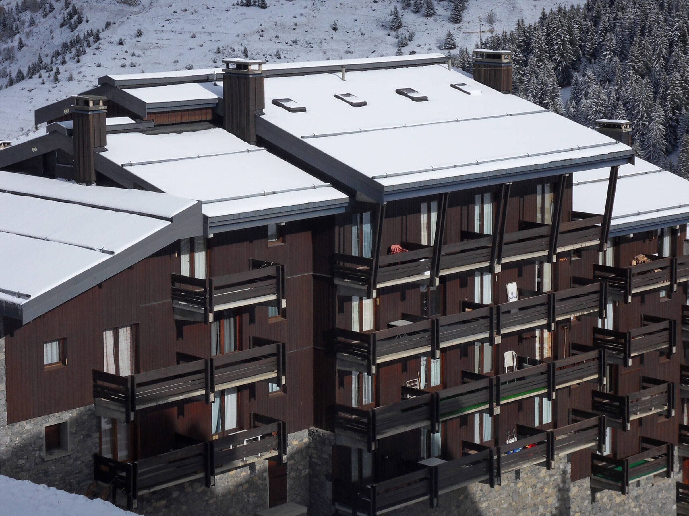 A multi-story building with a snow-covered roof, wooden balconies, and a mountainous backdrop.