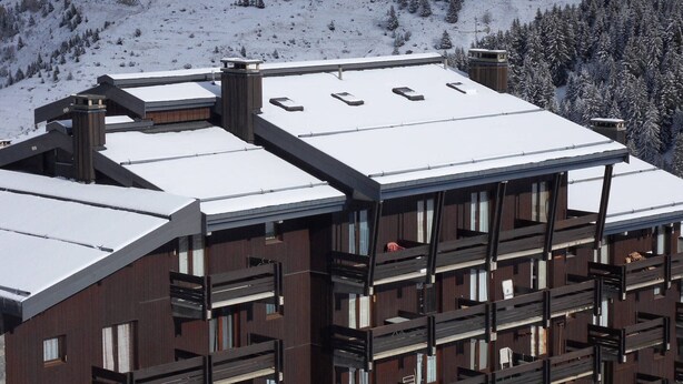 Een meerlaags gebouw met een sneeuwbedekte dak, houten balkon en een bergachtige achtergrond.