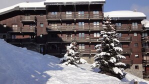 Een meerlaags hotel met balkons en een skipiste op de voorgrond.