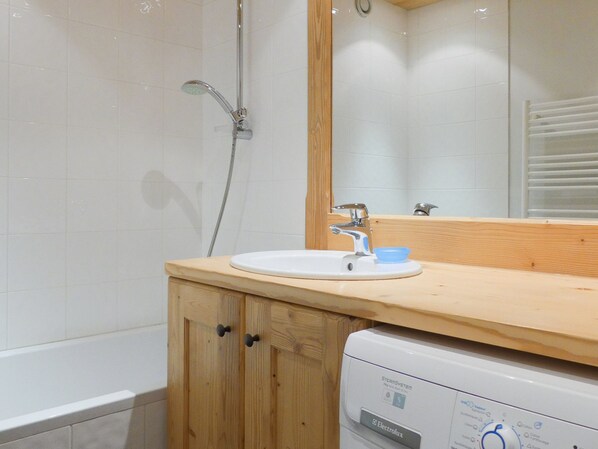A bathroom with a wooden cabinet, a white sink, a mirror, and a white washing machine. - Comfortable 3-room with fireplace, pets allowed in Méribel (Méribel)