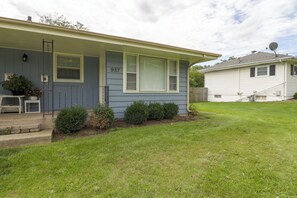Situated in a residential neighborhood, this single-story house features a well-maintained front yard and a welcoming front porch with a bench.