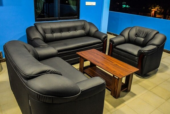 A room with a black leather sofa set, a wooden coffee table, and a blue accent wall.