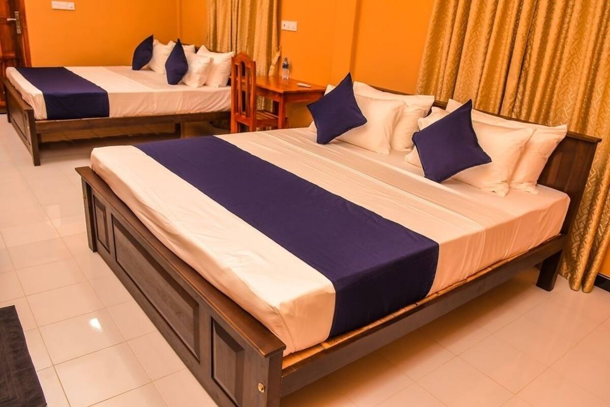 Une chambre d’hôtel avec deux lits simples, chacun doté d’un cadre en bois et de draps blancs. La chambre comprend également une petite table en bois et une chaise.