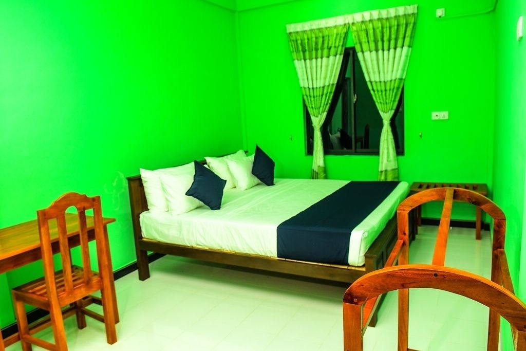A room with a bed, two chairs, and a window with curtains.