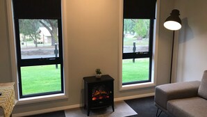 Ein Zimmer mit zwei Fenstern, einem Kamin, einer Couch und einer Lampe.