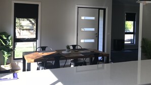 Eine moderne Küche mit einer großen Kochinsel, einem Essbereich mit Holztisch und Blick ins Freie.