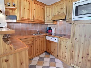A compact kitchen with wooden cabinets, a stainless steel sink, a dishwasher, and a microwave.