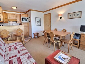 Una sala de estar acogedora con un sofá, una mesa de comedor con sillas, una zona de cocina con armarios de madera y un microondas, y un televisor sobre un mueble de madera.
