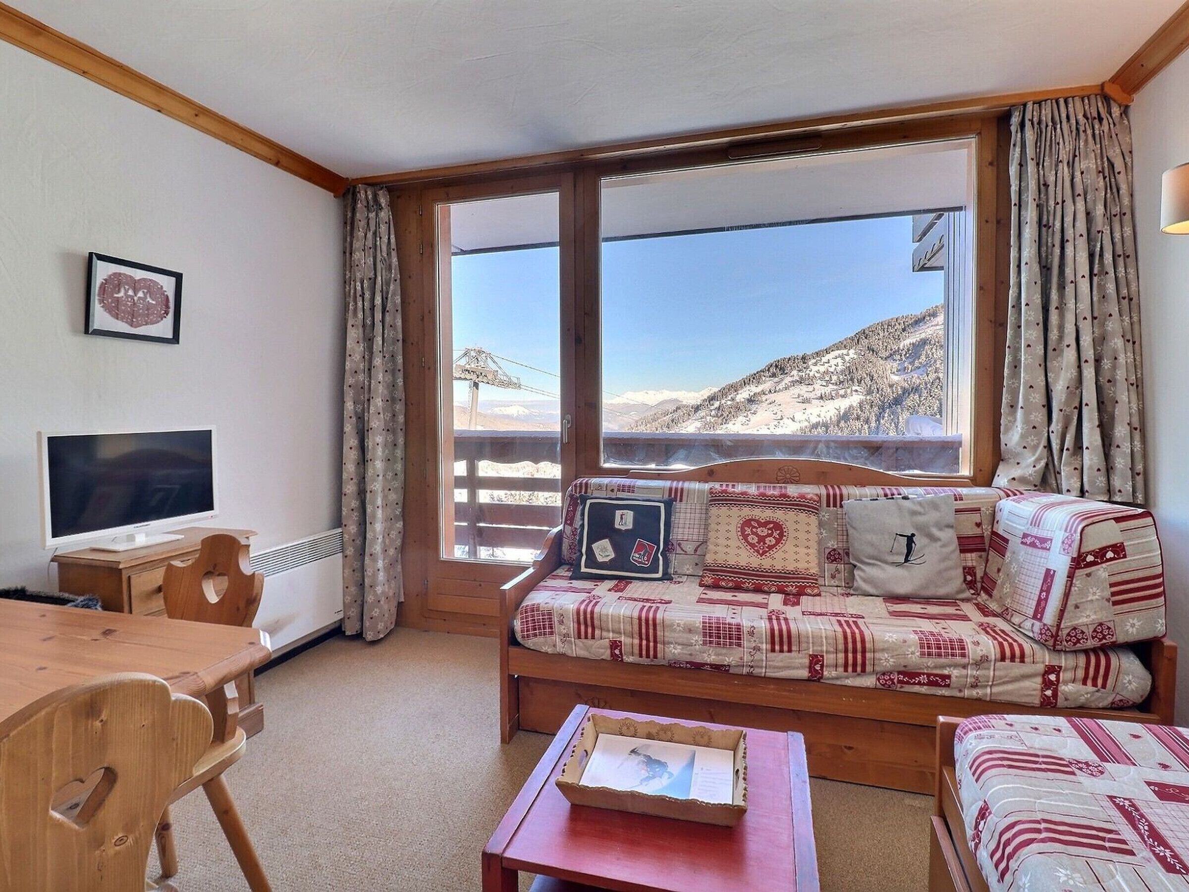 Een knus ingerichte kamer met een houten bureau, een flatscreen televisie, een bank met gestreepte kussens en uitzicht op een besneeuwd berglandschap door grote ramen.