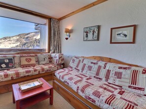 A cozy room with a wooden bench and sofa, a small table, and a window with a view of a snowy landscape.