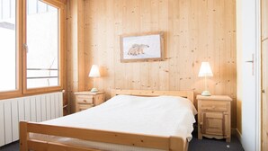 A wooden-paneled room with a bed, two bedside tables, a window, and a framed picture on the wall.
