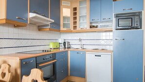 A compact kitchen with blue cabinets, a microwave, a dishwasher, and a stove.
